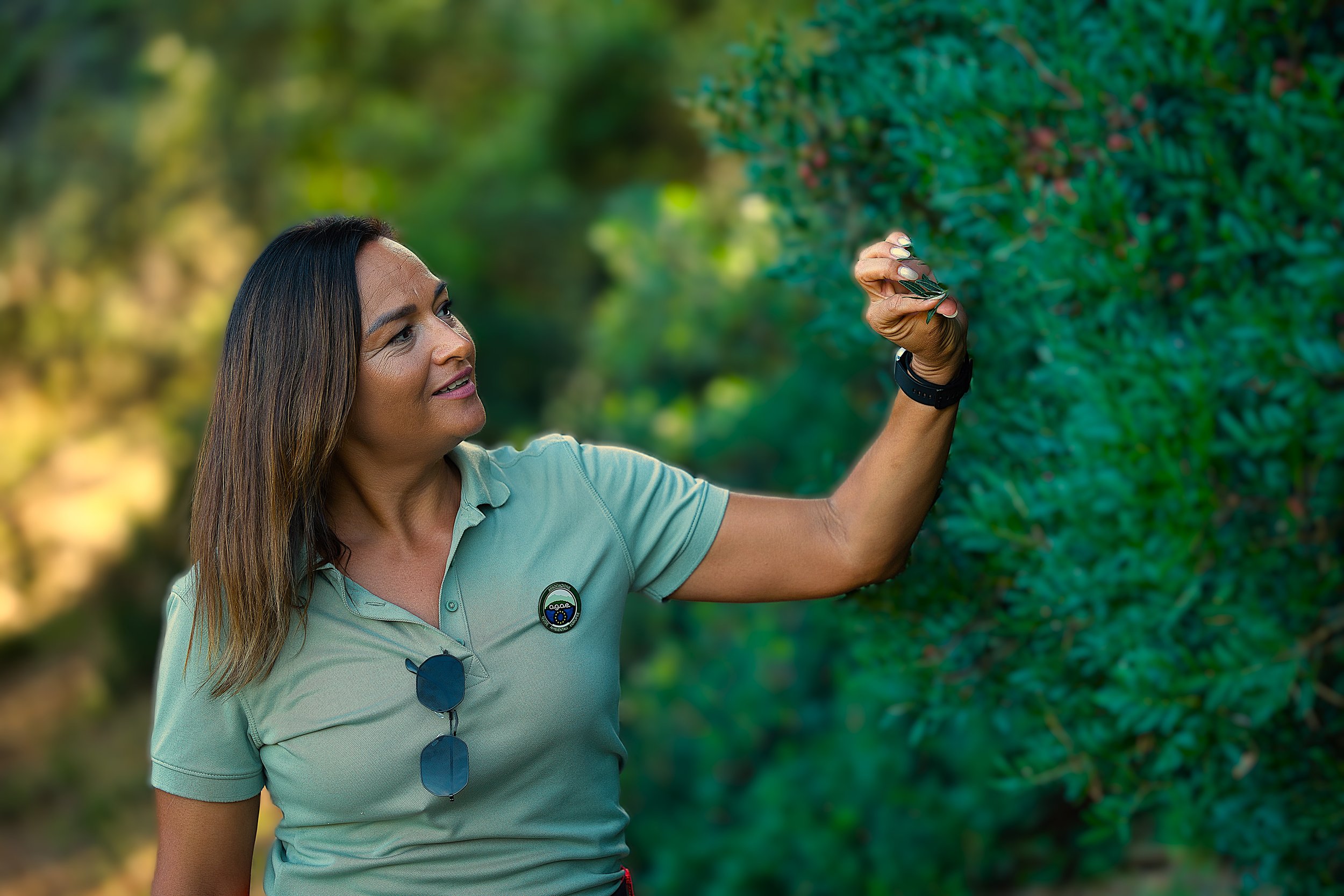 Una donna che osserva e tocca un ramoscello di foglie in un ambiente naturale con vegetazione verde.