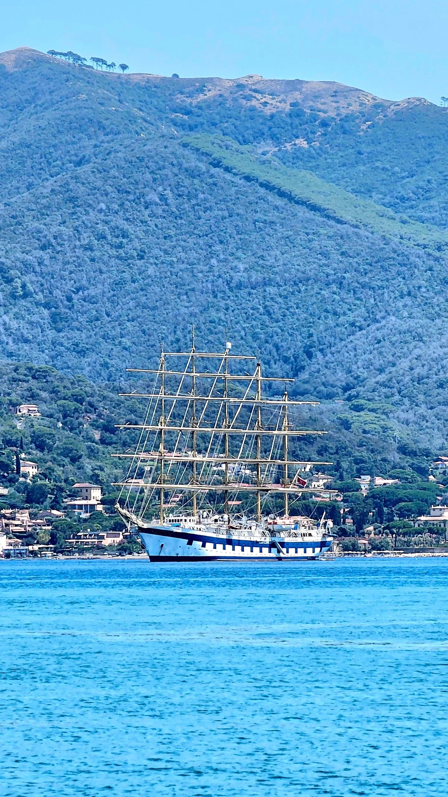 Una nave a tre alberi in mare con montagne verdi sullo sfondo.