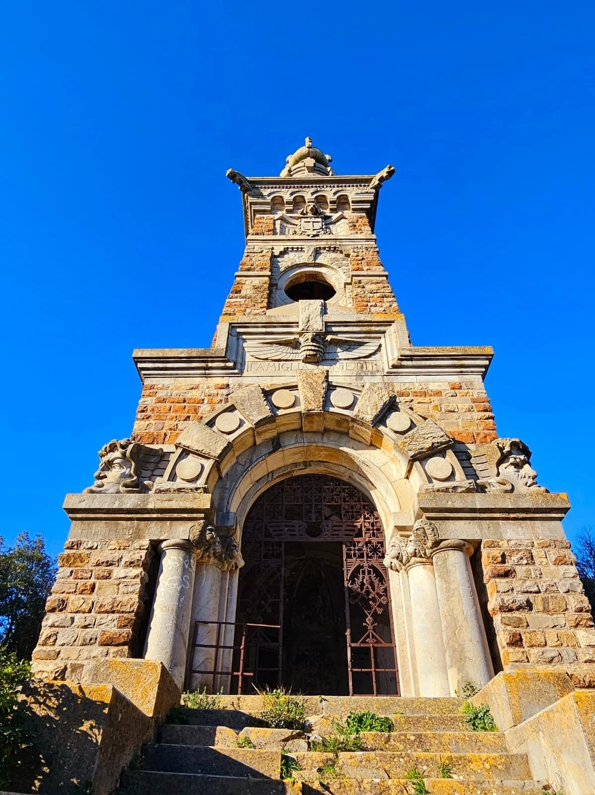 Vista di un vecchio campanile in pietra con sculture di leoni e dettagli architettonici, sotto un cielo blu.