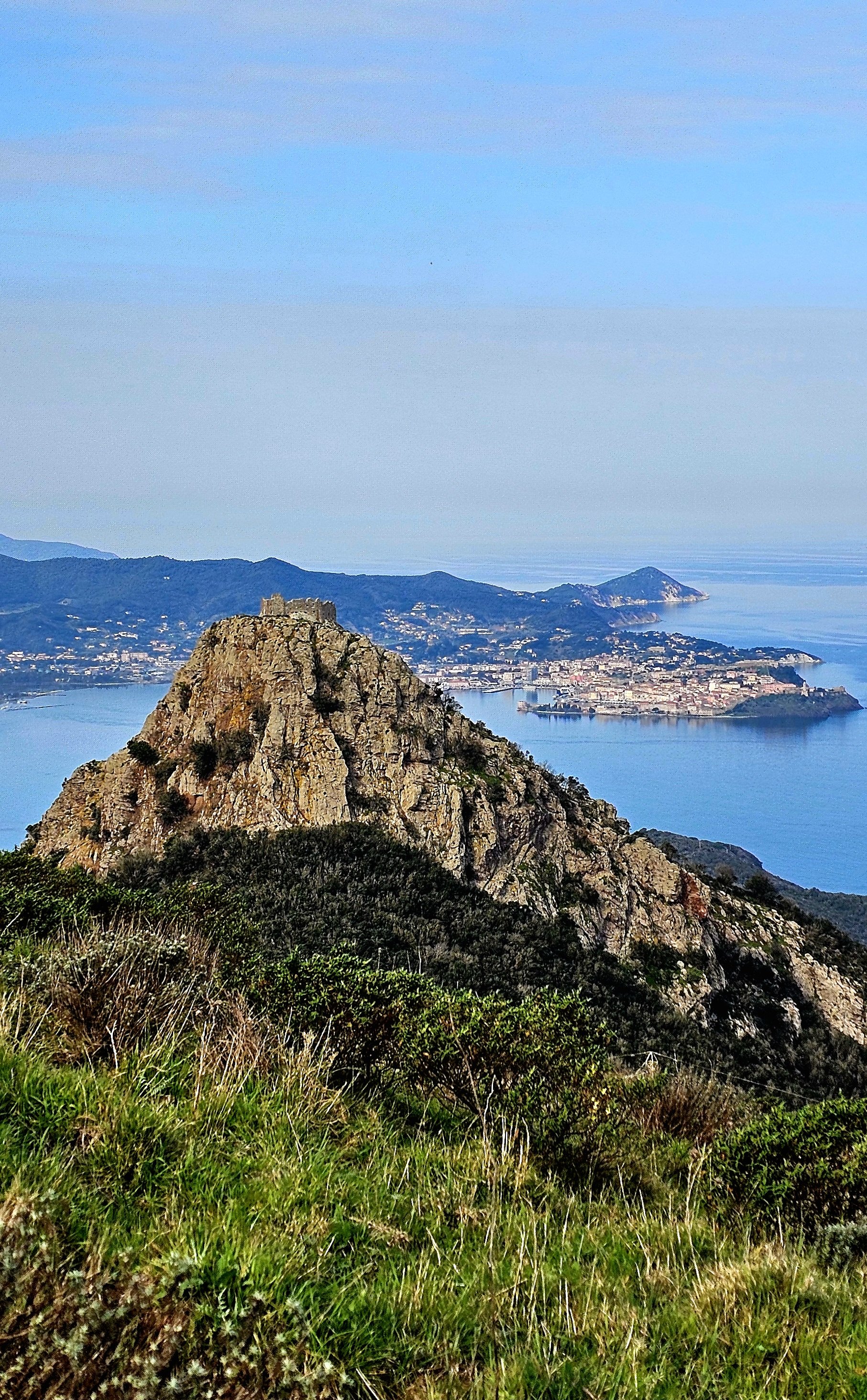 Paesaggio con una montagna rocciosa e una vista sul mare e una città costiera in lontananza.