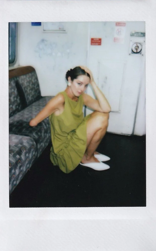 A woman in a green dress and white shoes sitting on the floor next to a patterned sofa, in a room with white walls and a white door.