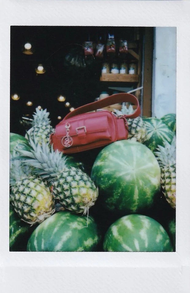 Display of fresh pineapples and watermelons with a red purse on top, in a market or produce stand setting.