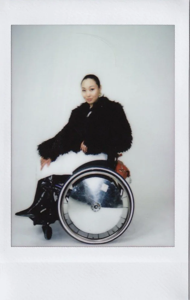 A woman in a black coat sitting in a wheelchair with a clock in front of her