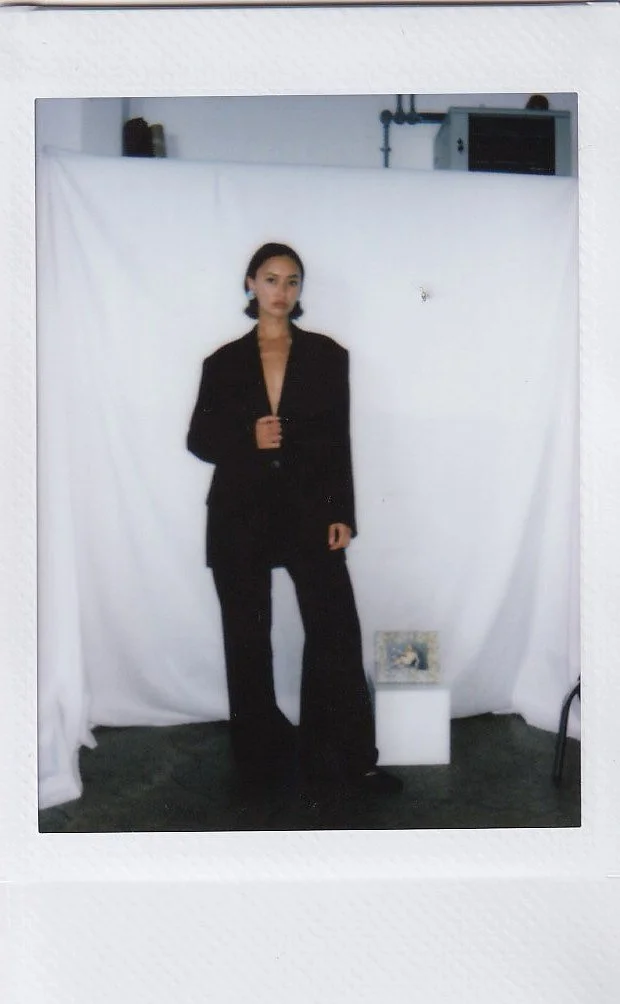A woman in a black suit standing in front of a white backdrop in a photography studio.