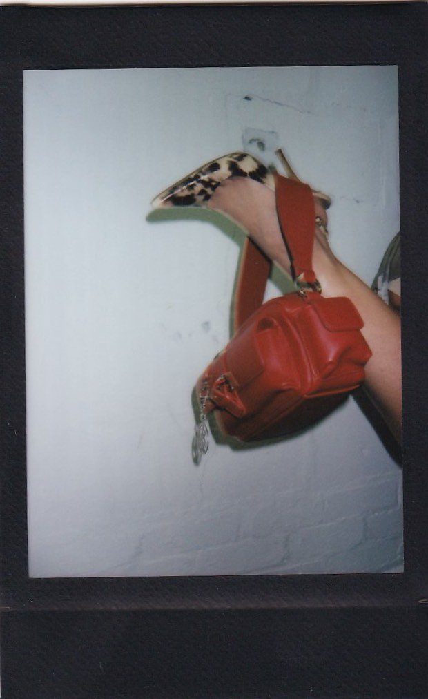 A wall decor piece resembling a bird's head and neck, with a red bag hanging from it, all mounted on a white wall.