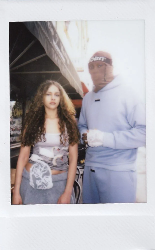 A young woman with long curly hair and a young man wearing a ski mask and gloves standing outdoors.