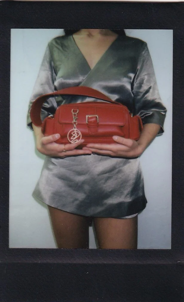 A woman wearing a gray satin dress holding a small red handbag with a gold keychain