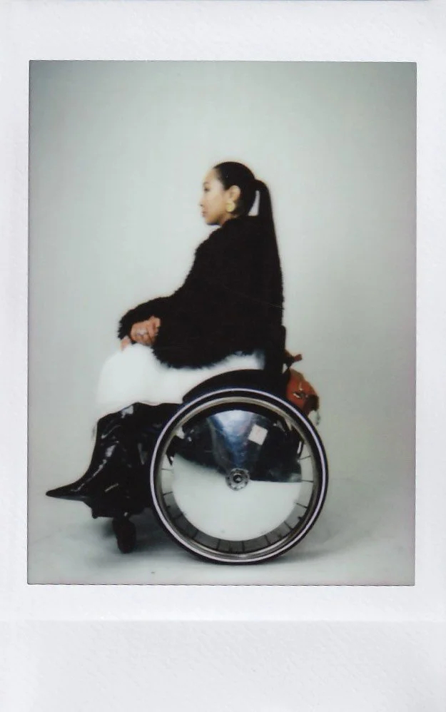 Side view of a woman sitting in a wheelchair against a plain background.