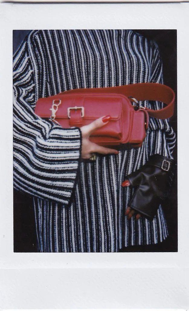 Person wearing a black and white striped cardigan holding a red handbag and wearing black fingerless gloves with red nail polish.