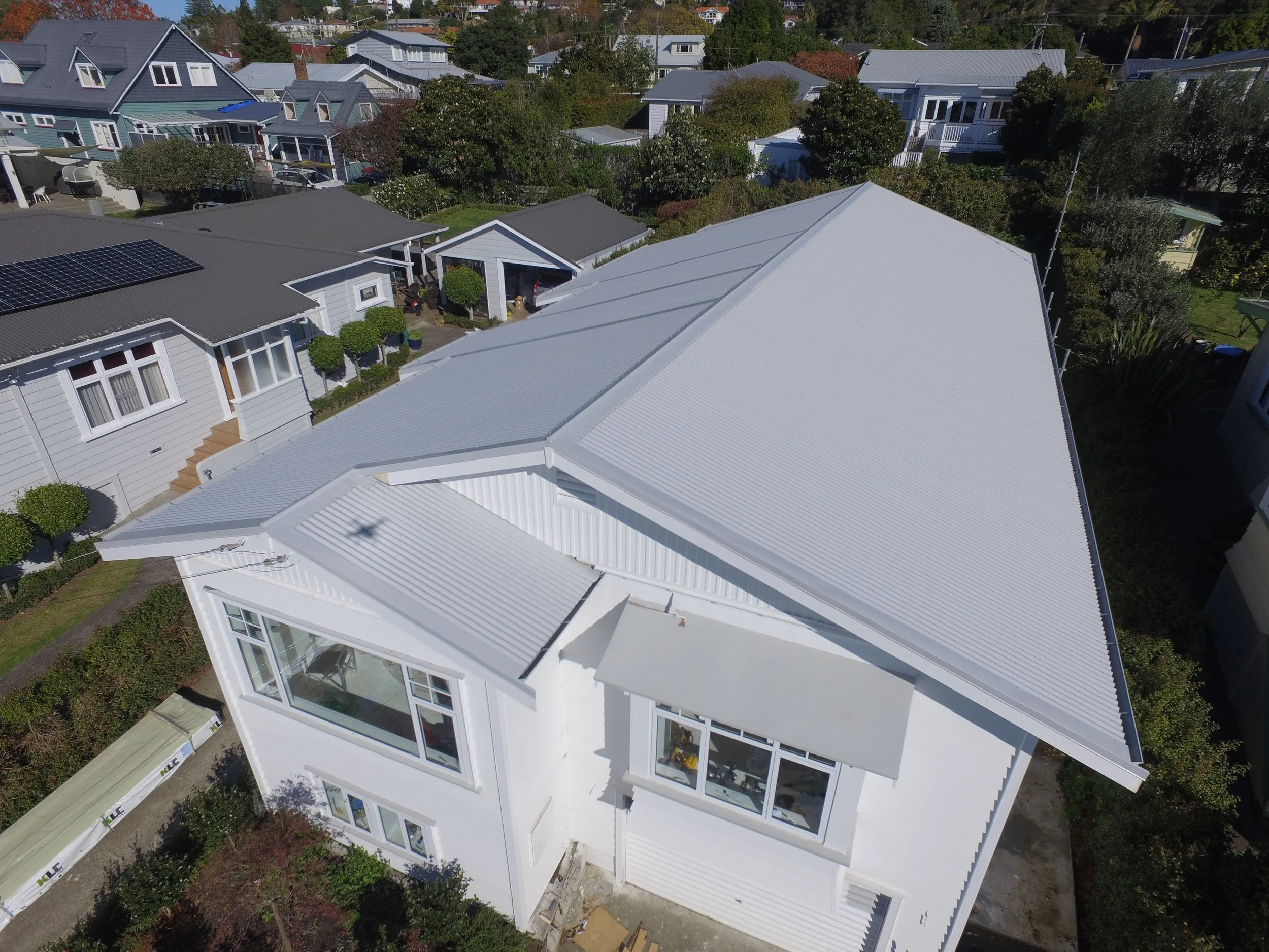 Aerial view of a white house with a metal roof in a neighborhood with other houses and trees.