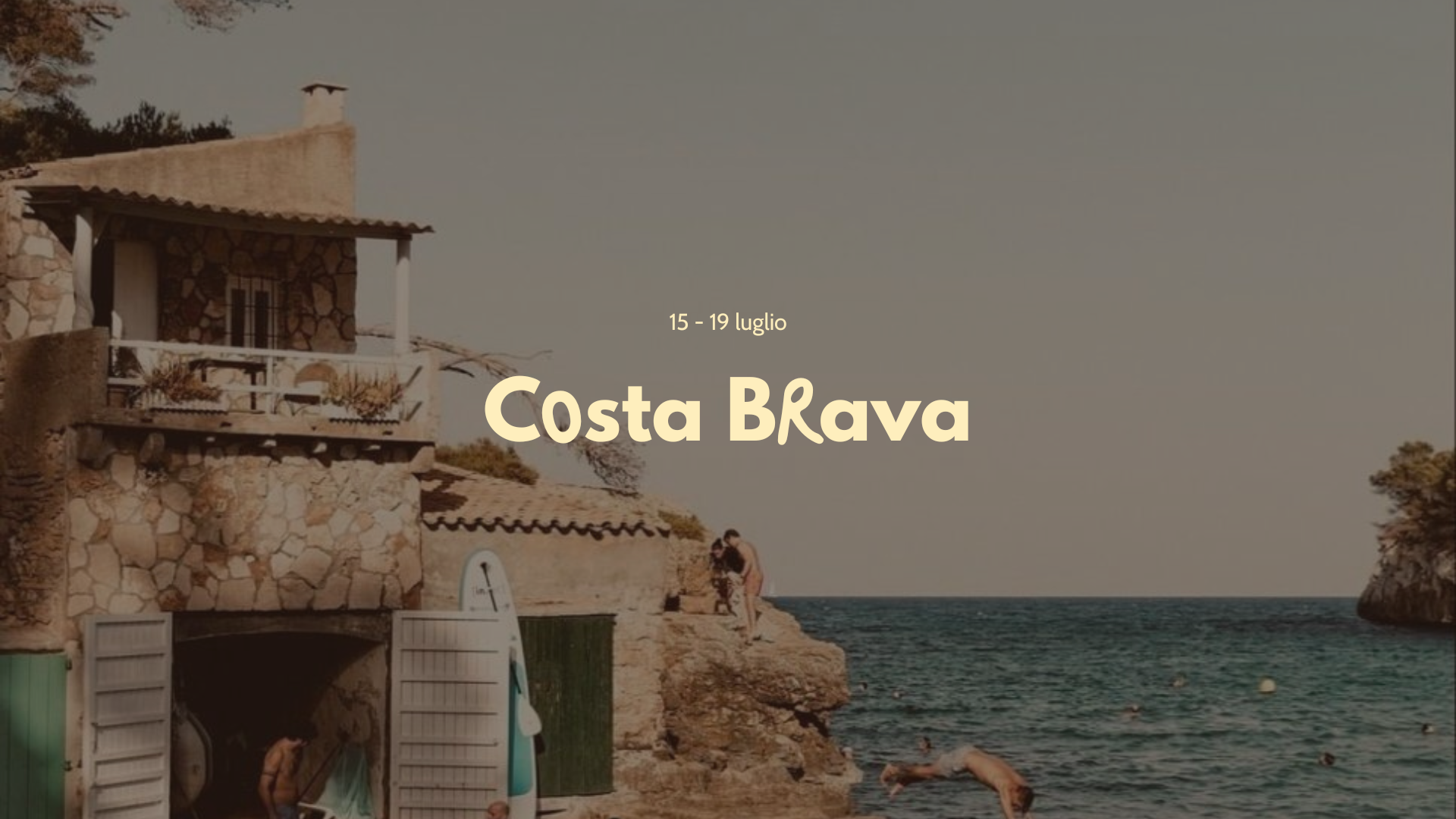 Scorcio della Costa Brava con case in pietra, vista sul mare, persone che si rilassano vicino alla spiaggia e una giovane che si tuffa in acqua.