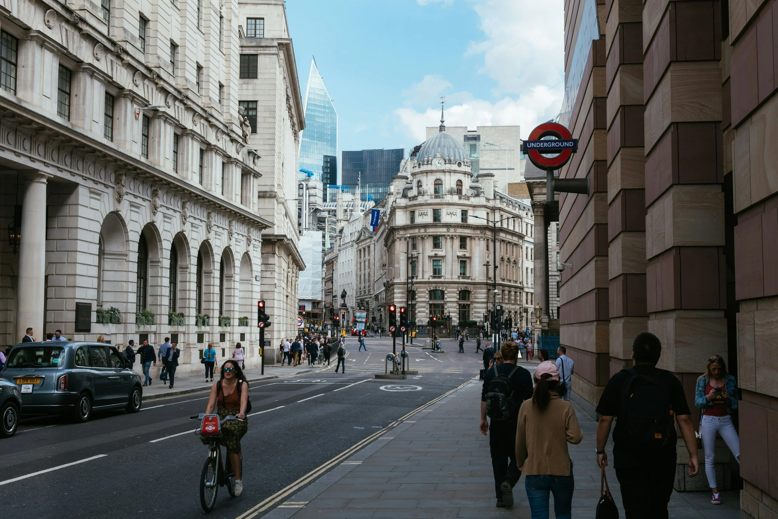 A bustling street in Bank, London shows cyclists and walkers meandering through the city.