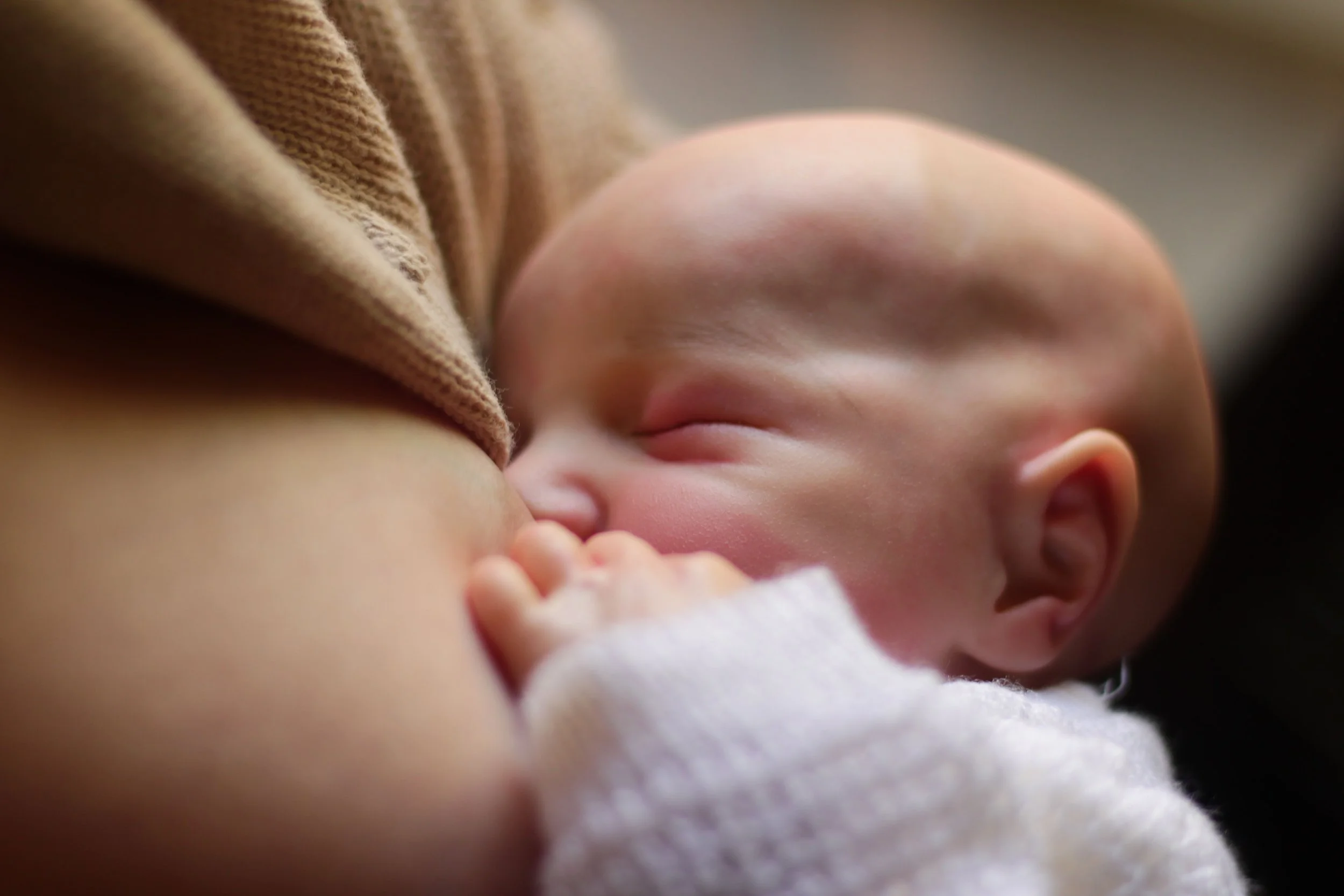 Nahaufnahme eines schlafenden Babys, das an der Brust einer Mutter nuckelt.