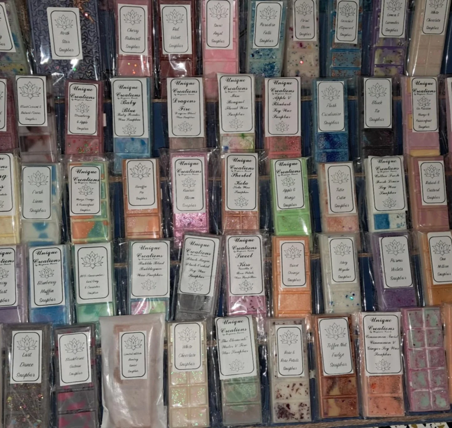 Display of various scented wax melts in packaged trays with labels.