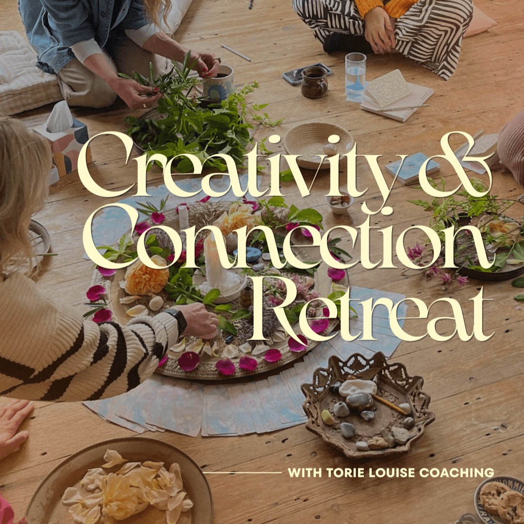 A group of people sitting on the floor around a table with flowers and decorative items, engaged in a creative activity during a retreat.