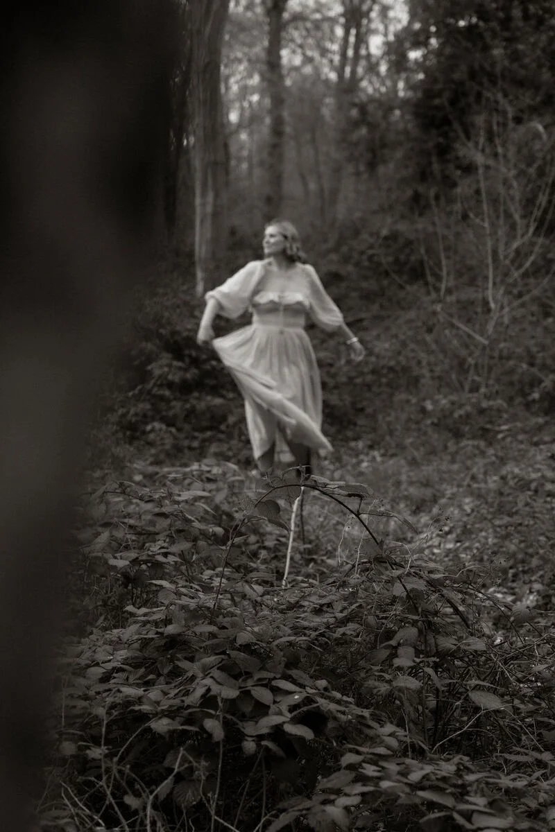 A woman in a flowing dress walking through a wooded forest area.