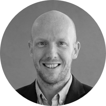 A smiling man with short hair and a collared shirt, in a black and white photo.