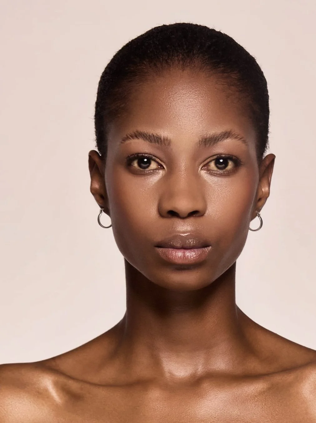 Close-up portrait of MOGALADI Leso from AURA Models with short natural hair, minimal makeup, wearing small hoop earrings, and looking directly at the camera against a plain light background.