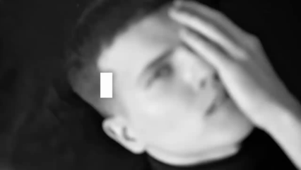 A young man with short dark hair looking at the camera, covering part of his face with one hand, all in black and white.