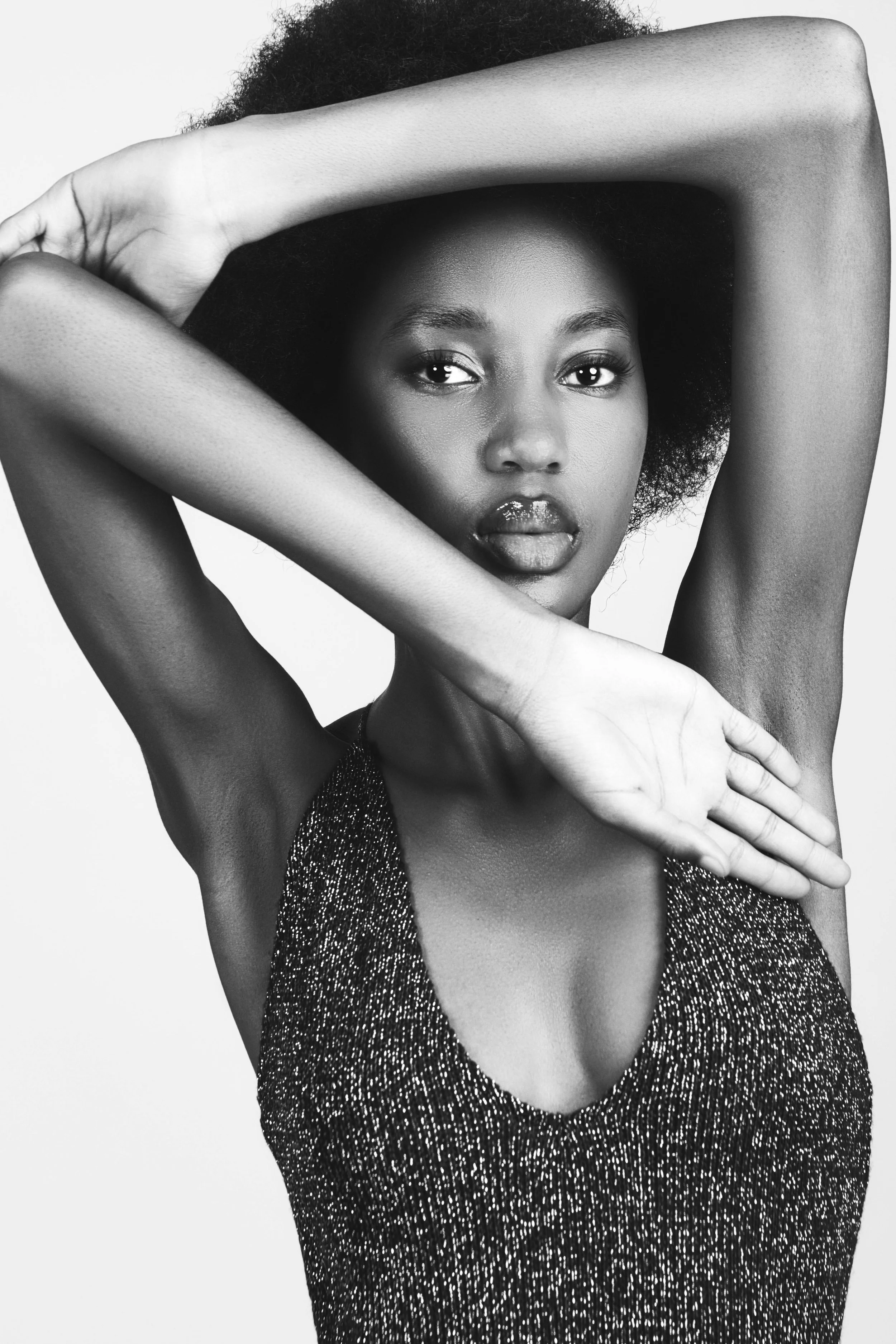 A black-and-white photograph of RORY Merafe from AURA Models with natural hair, wearing a sparkly dress, posing with arms crossed around her face.