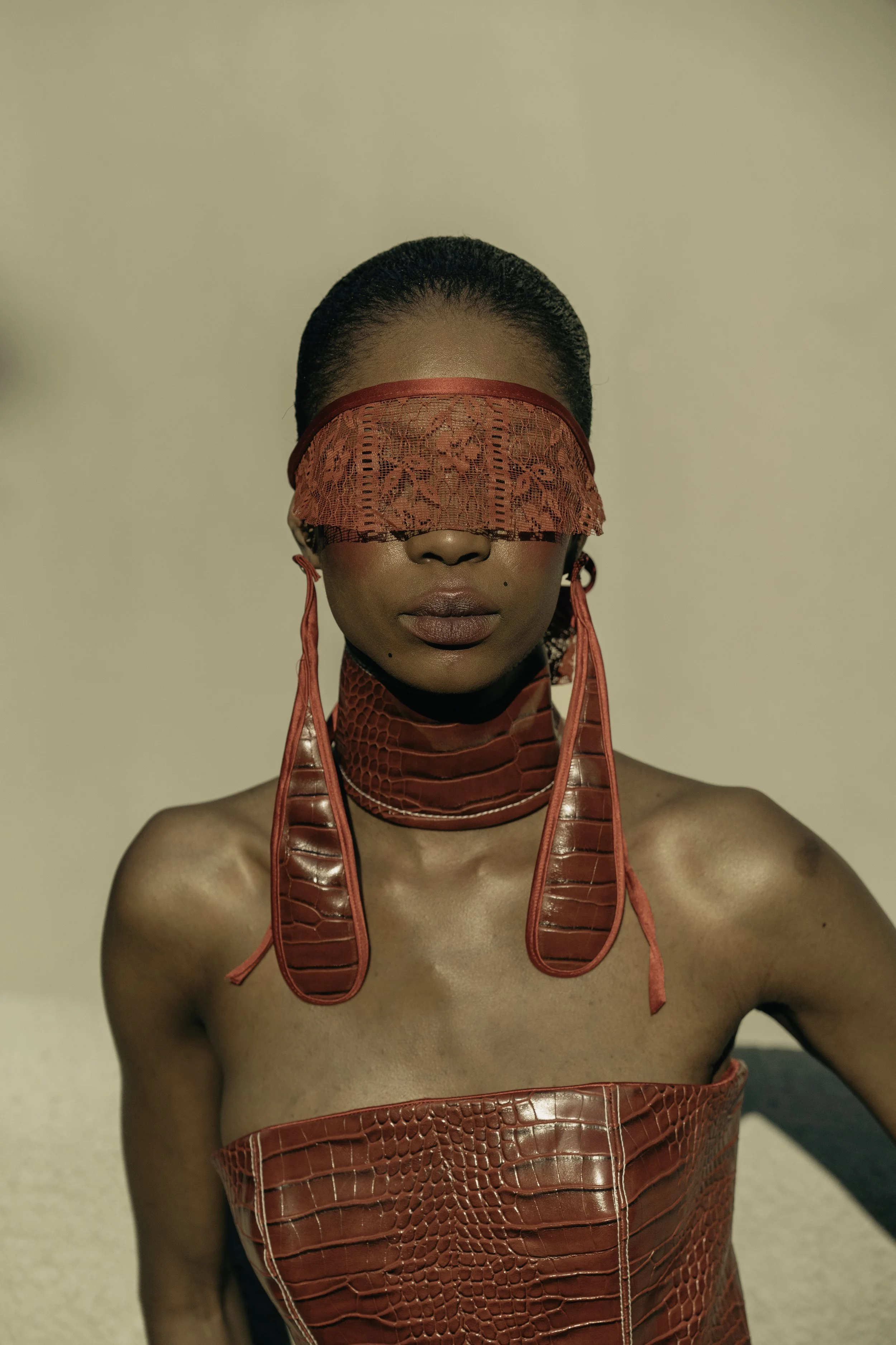 MOGALADI Leso from AURA Models with dark skin, short hair, and full lips wearing a red lace blindfold and red fashion accessories, with a blurred background.