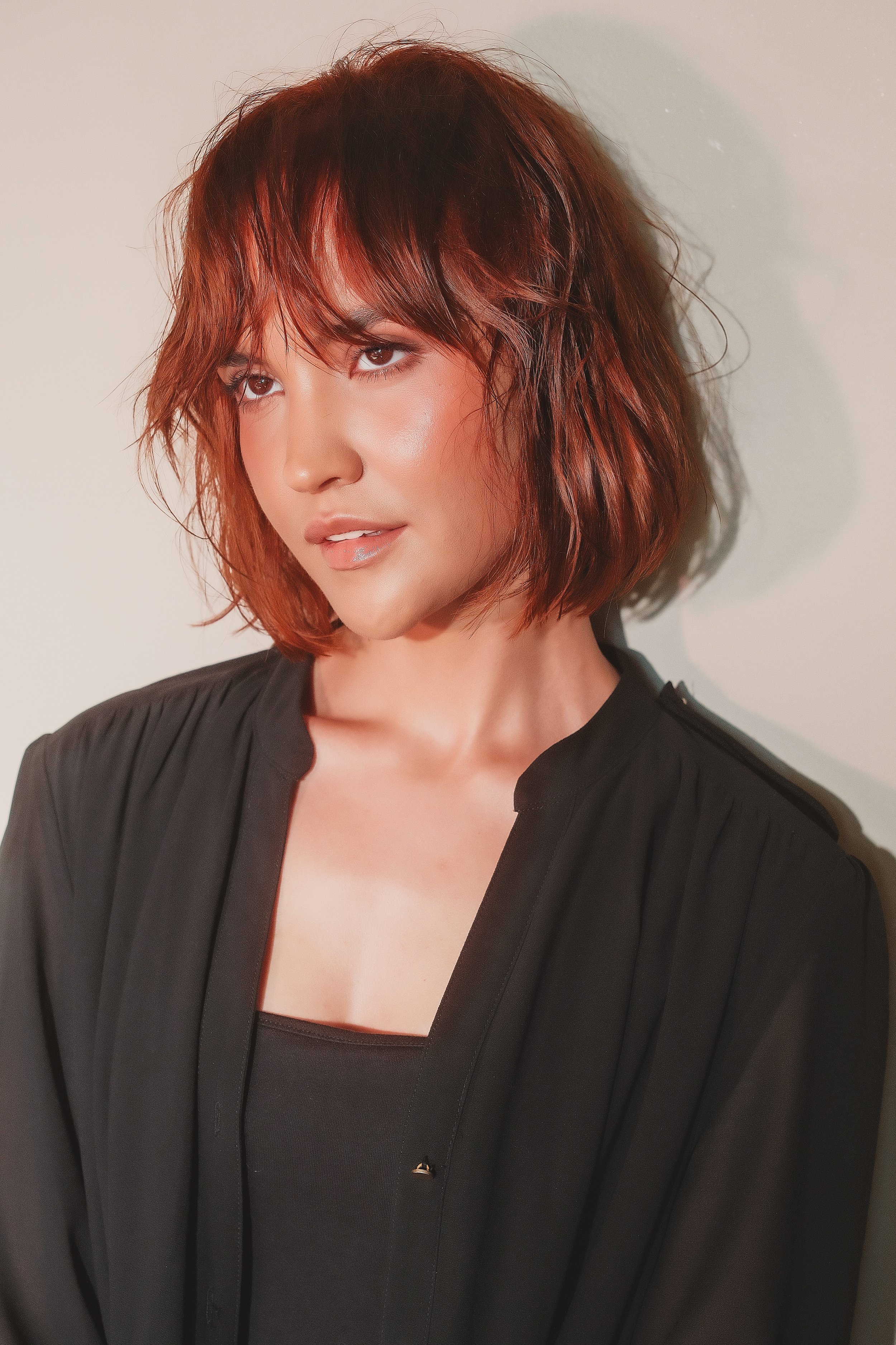 MARINET Potgieter from AURA Models Urban with auburn, wavy, shoulder-length hair, wearing a black blazer and top, looking to the side against a white background.