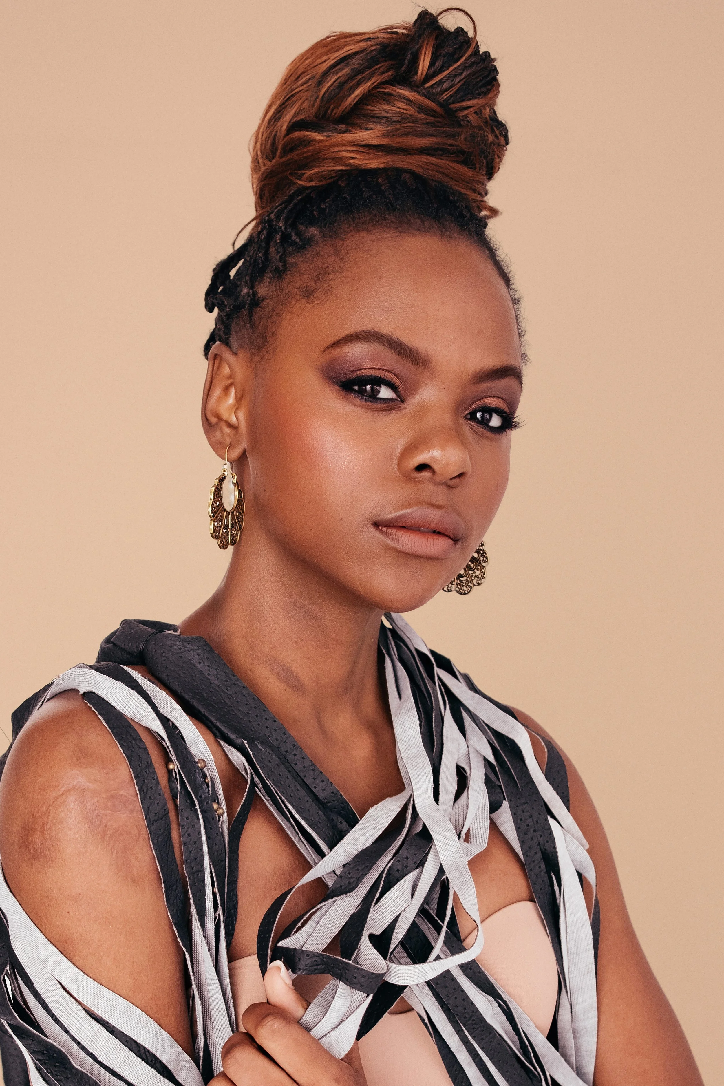 Portrait of a woman with styled hair, wearing earrings, beige top, and a black and white striped draped fabric.