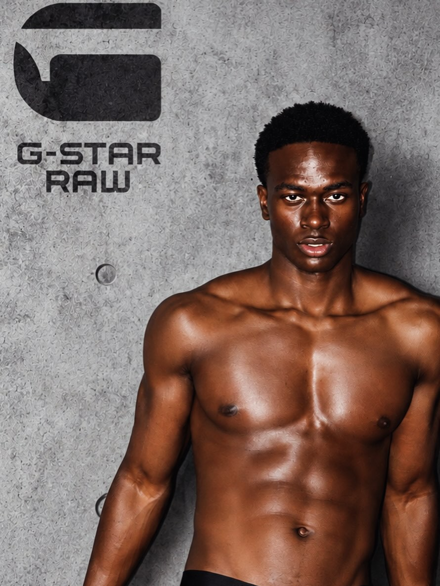 MBHURI Baloyi from AURA Models with dark skin and short curly hair standing against a gray textured wall with the G-STAR RAW logo.