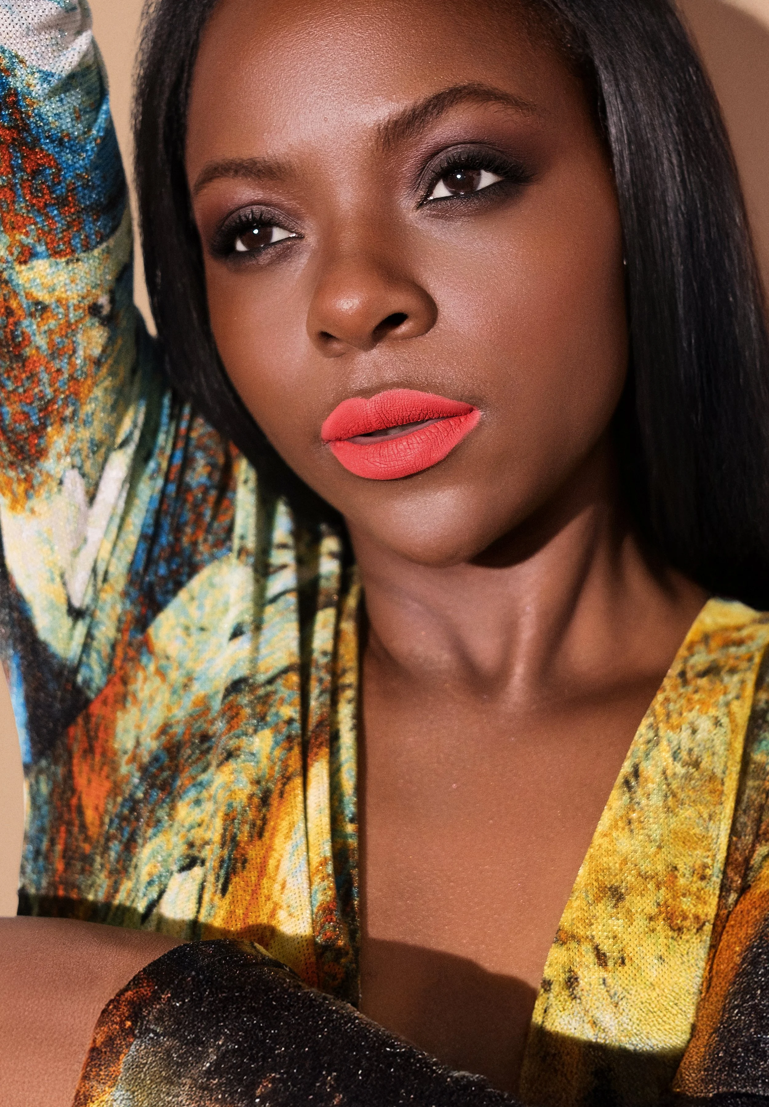 Close-up of a woman with dark skin, black hair, wearing vibrant makeup including red lipstick and dark eye makeup, dressed in a colorful, patterned top.