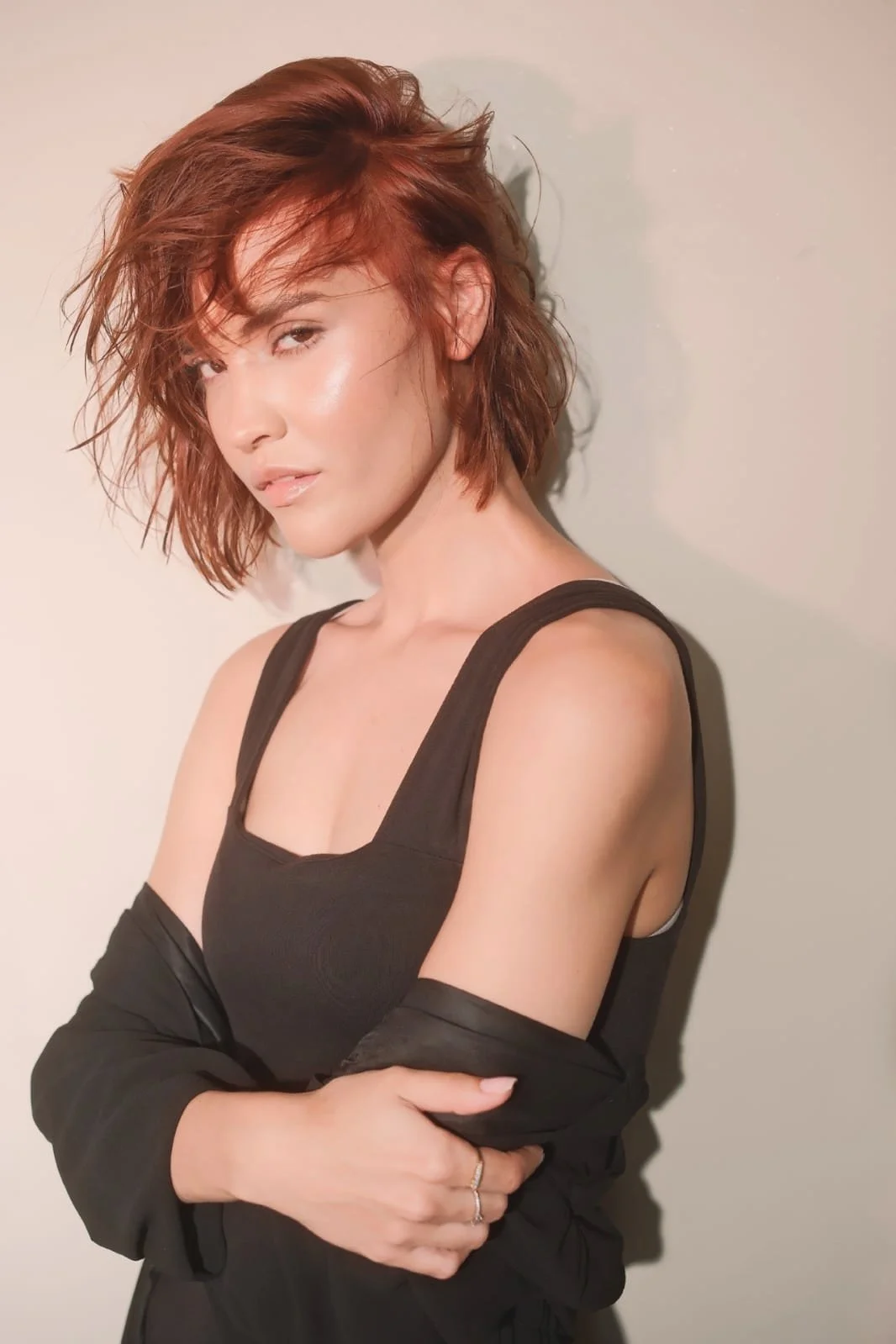 MARINET Potgieter from AURA Models Urban with short, tousled red hair and fair skin stands against a plain background. She is wearing a black tank top and a black jacket draped over her arms. 