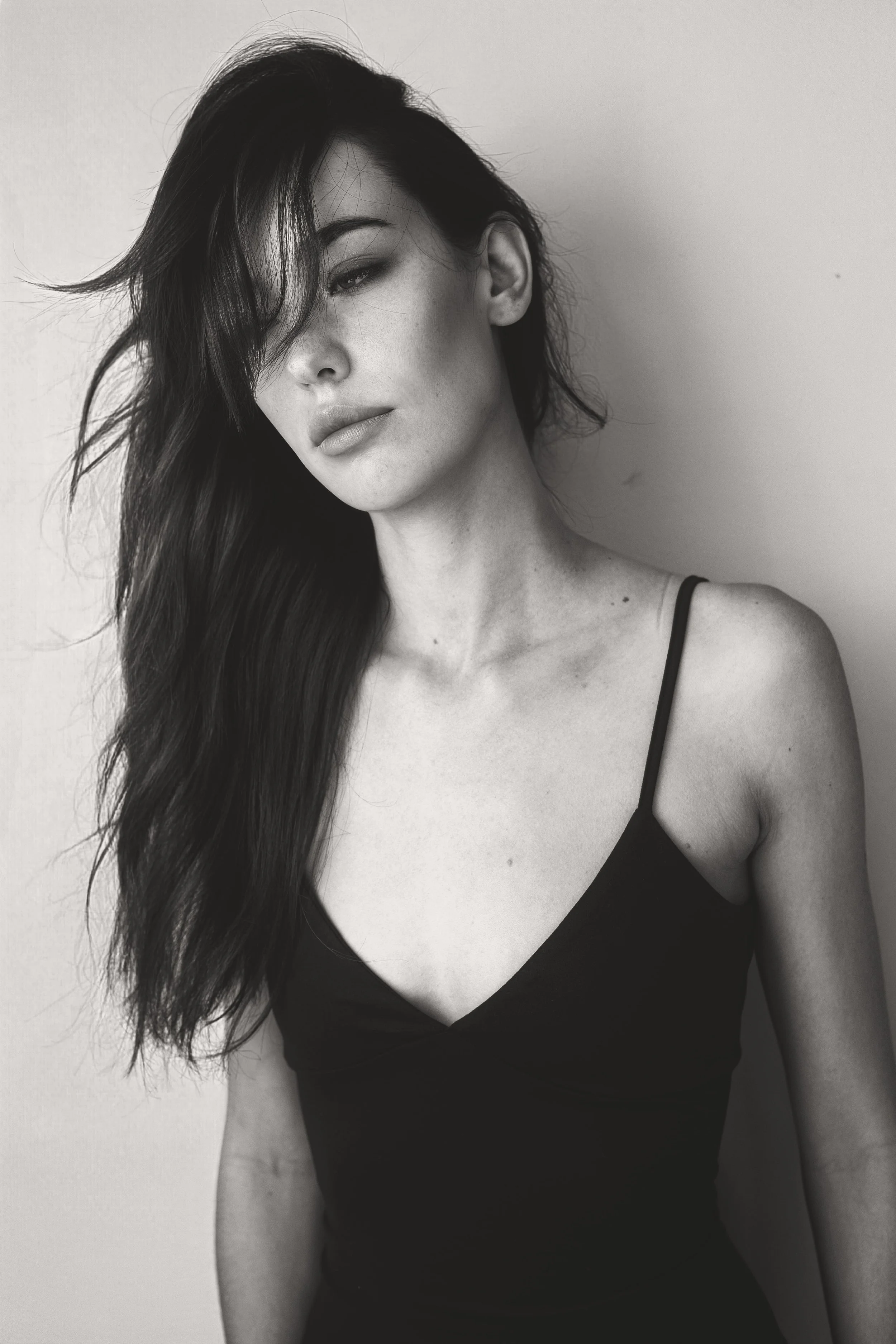 Black and white photograph of MONIQUE van Loggerenberg from AURA Models with long hair and a black spaghetti strap top, partially covering her face with her hair, looking slightly to the side.