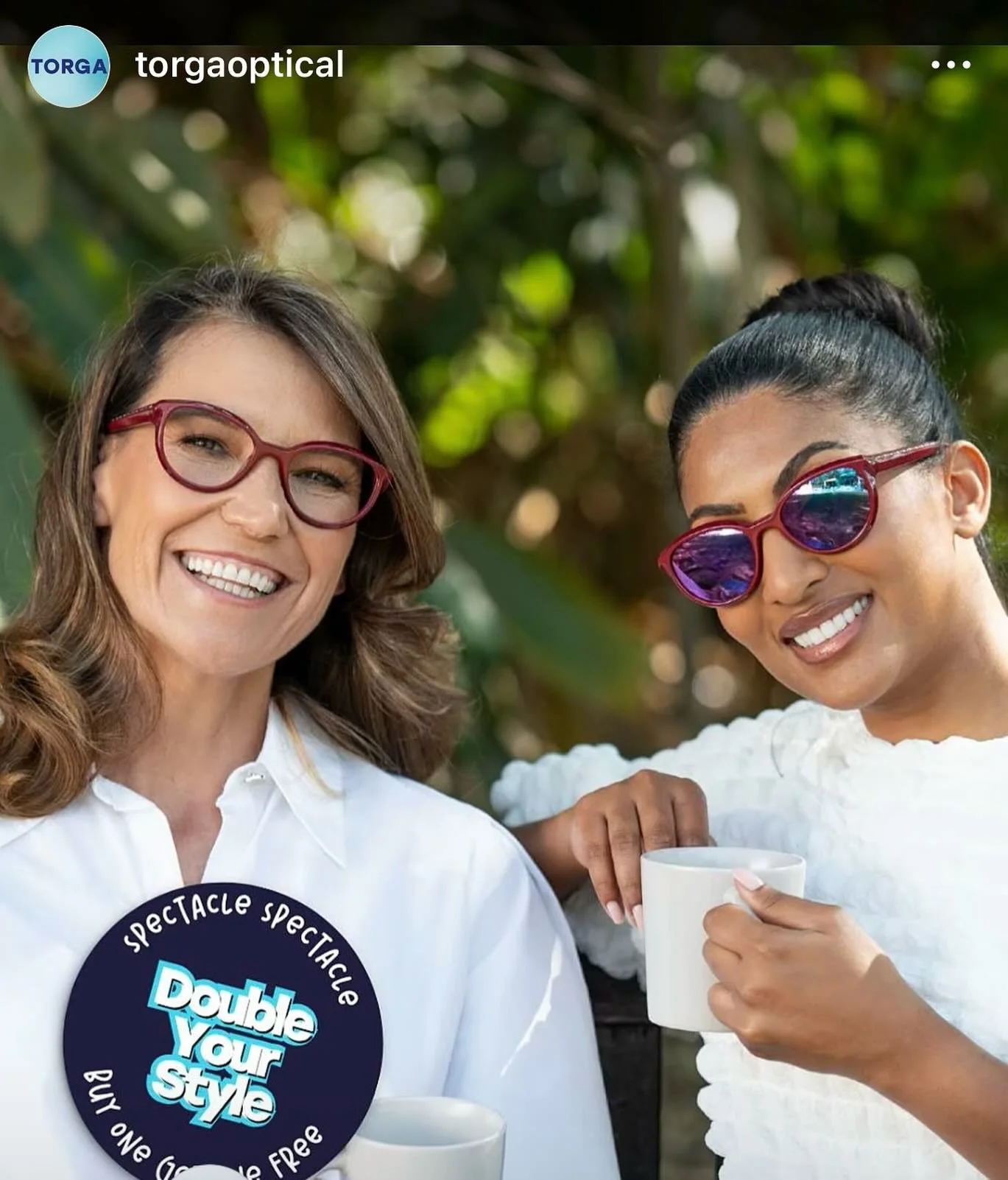 DESIRE Campbell from AURA Models and another girl outdoors, smiling, wearing colorful sunglasses and white tops, holding coffee mugs, with green leafy background. Torga Eyewear