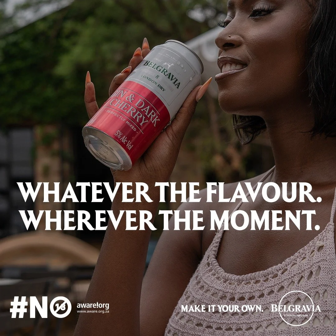 ONA Constantin from AURA Models with dark skin and black hair holding a can of Belgravia gin and cherry flavor near her face, smiling with her tongue slightly out, outdoors with trees in the background.