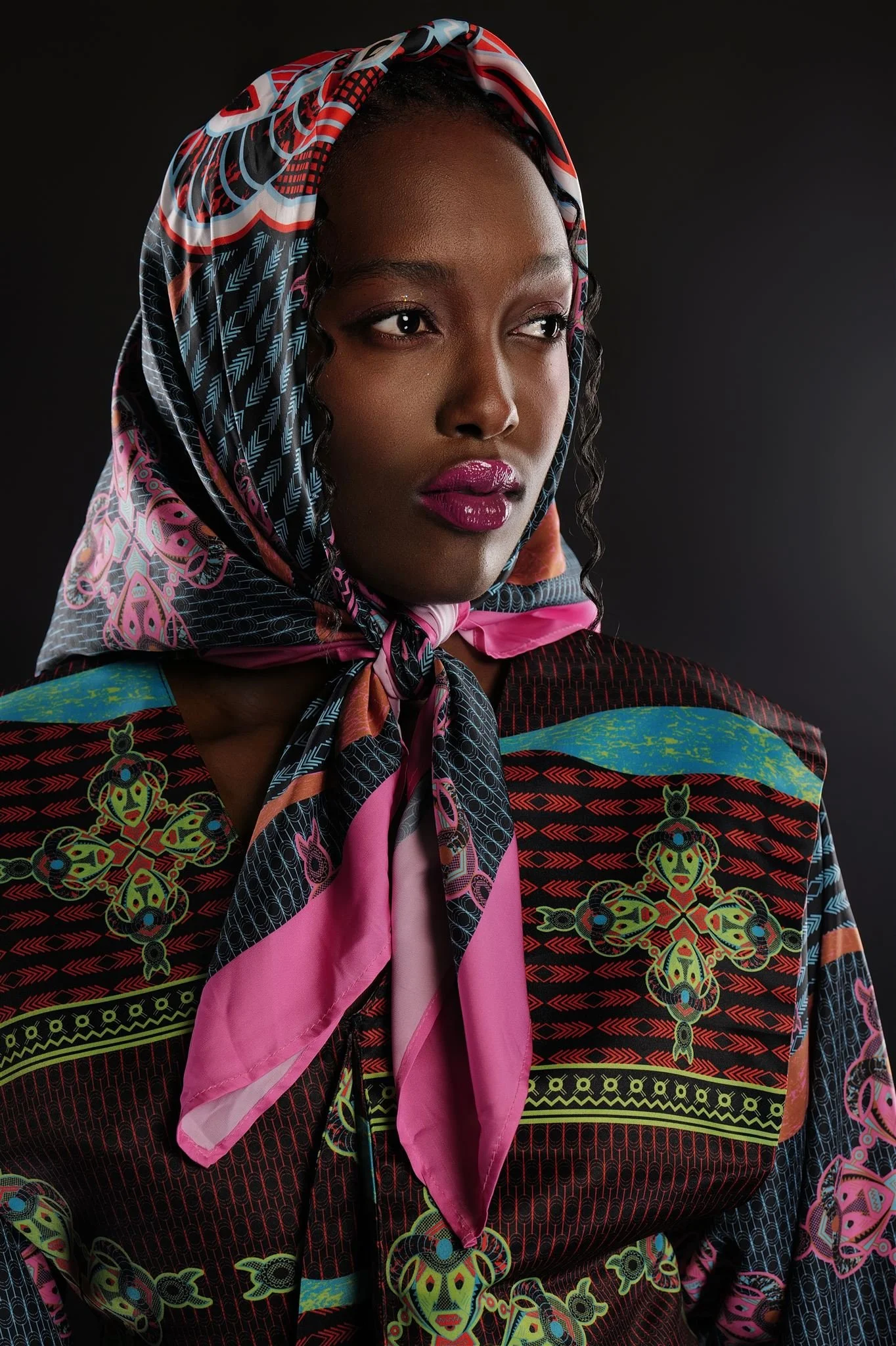 KIM Chakanyuka from AURA Models wearing a colorful, patterned Masamara headscarf and matching clothing with intricate designs, set against a dark background.