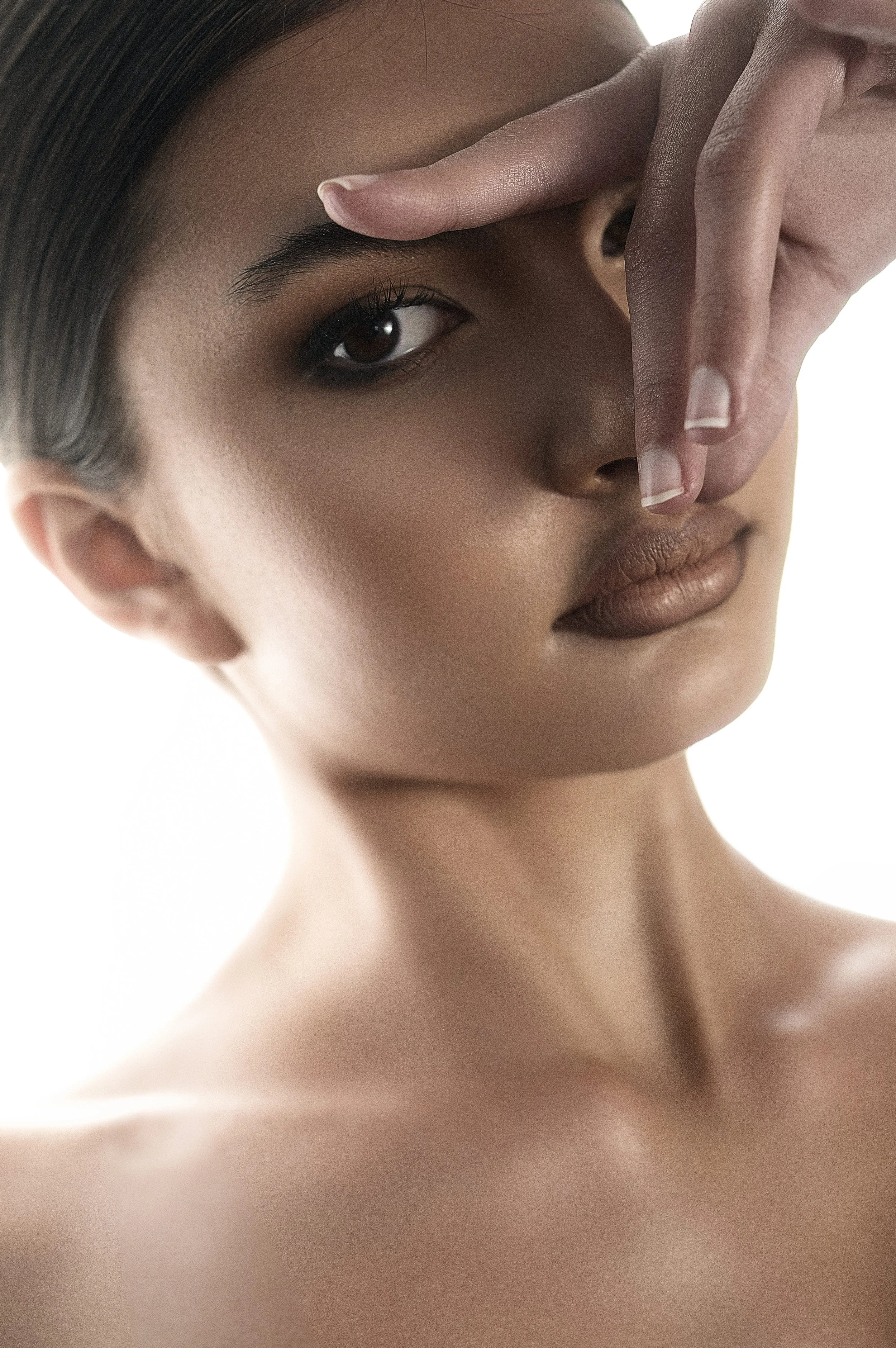 Close-up of a KEIRA Louw from AURA Models face and neck, with one hand partially covering her face, focusing on her eye and lips.