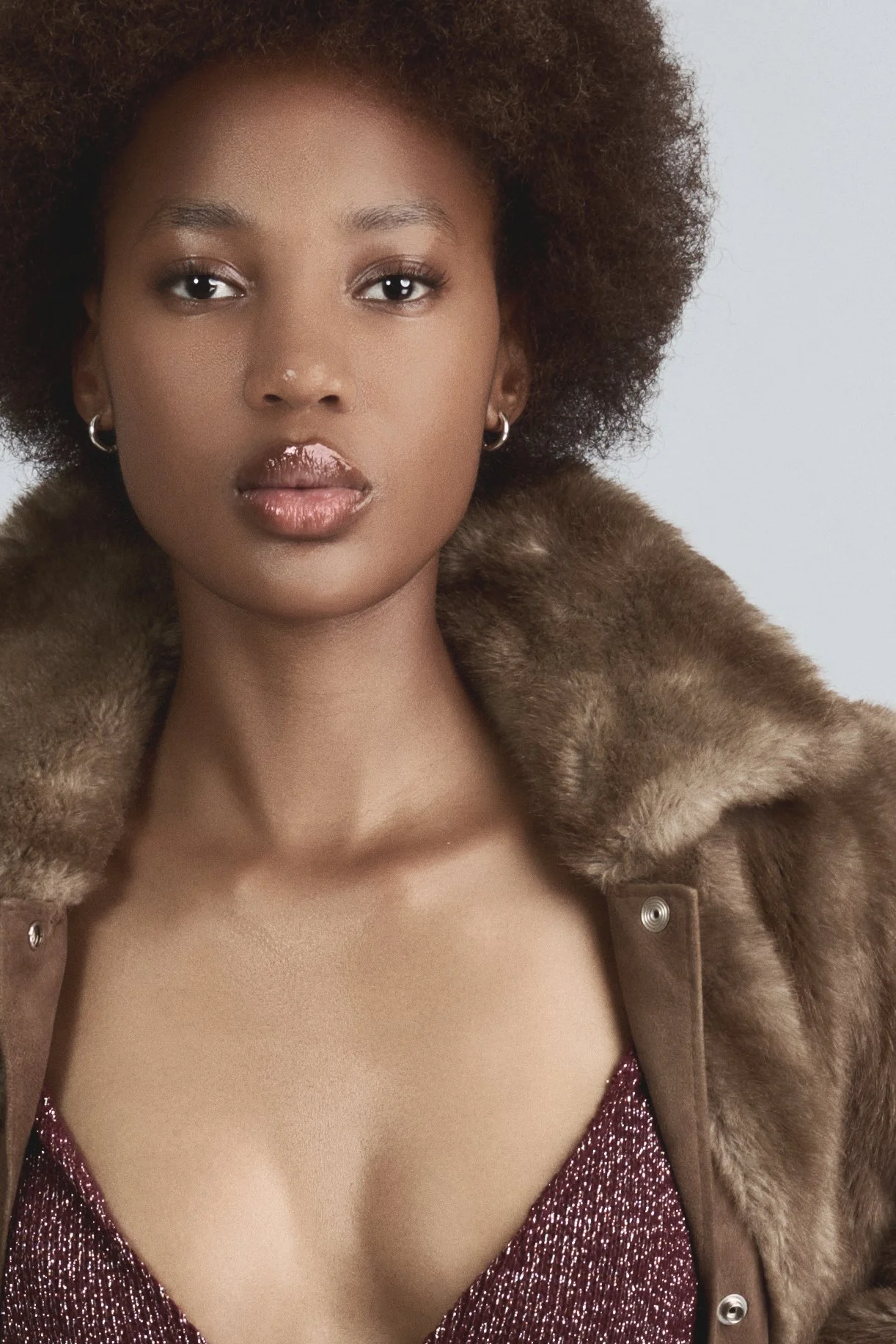 RORY Merafe from AURA Models with curly brown hair and hoop earrings, wearing a fur-lined coat over a sparkly burgundy dress.