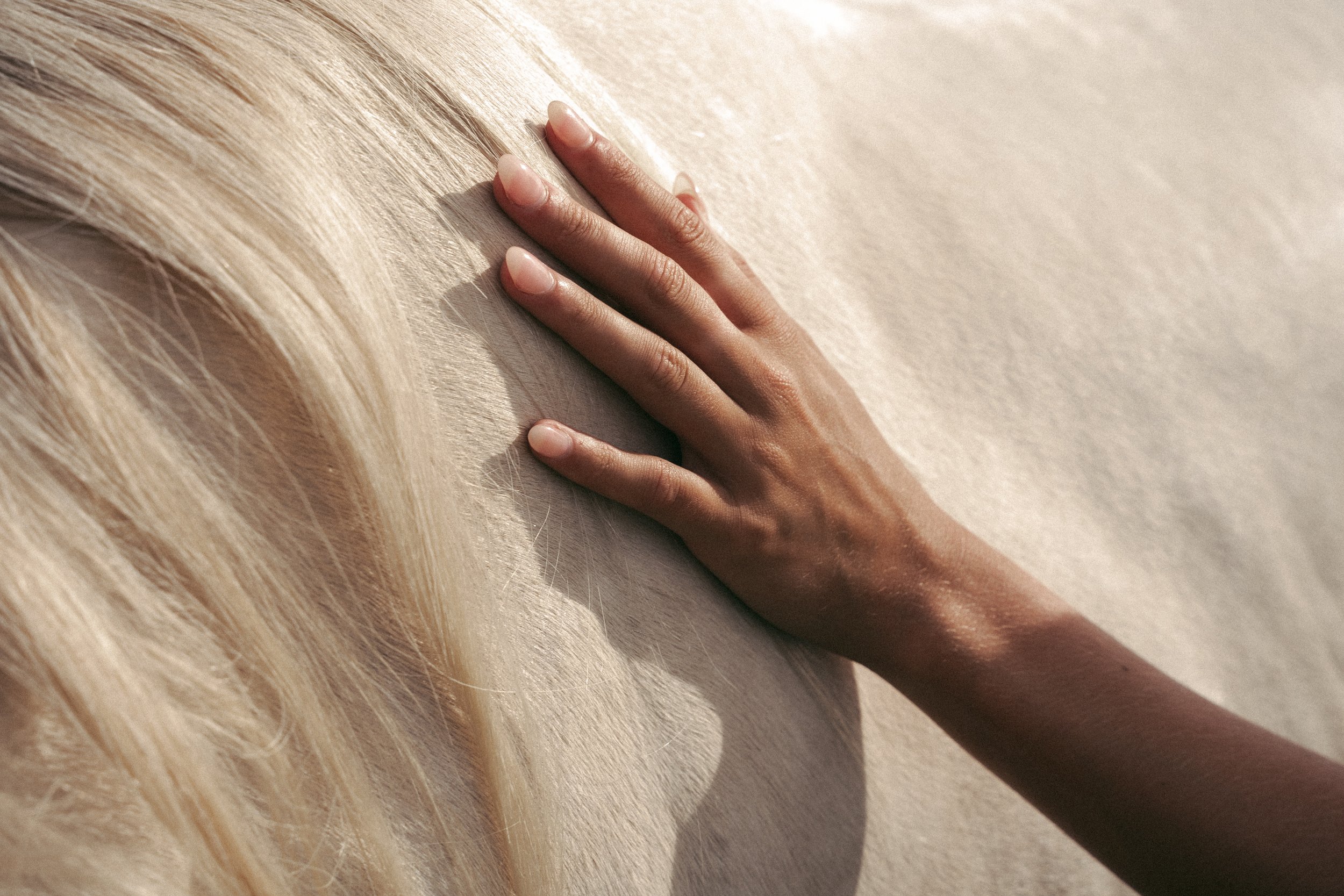 Close-up of a hand gently touching a sandy surface, with blonde hair in the background.
