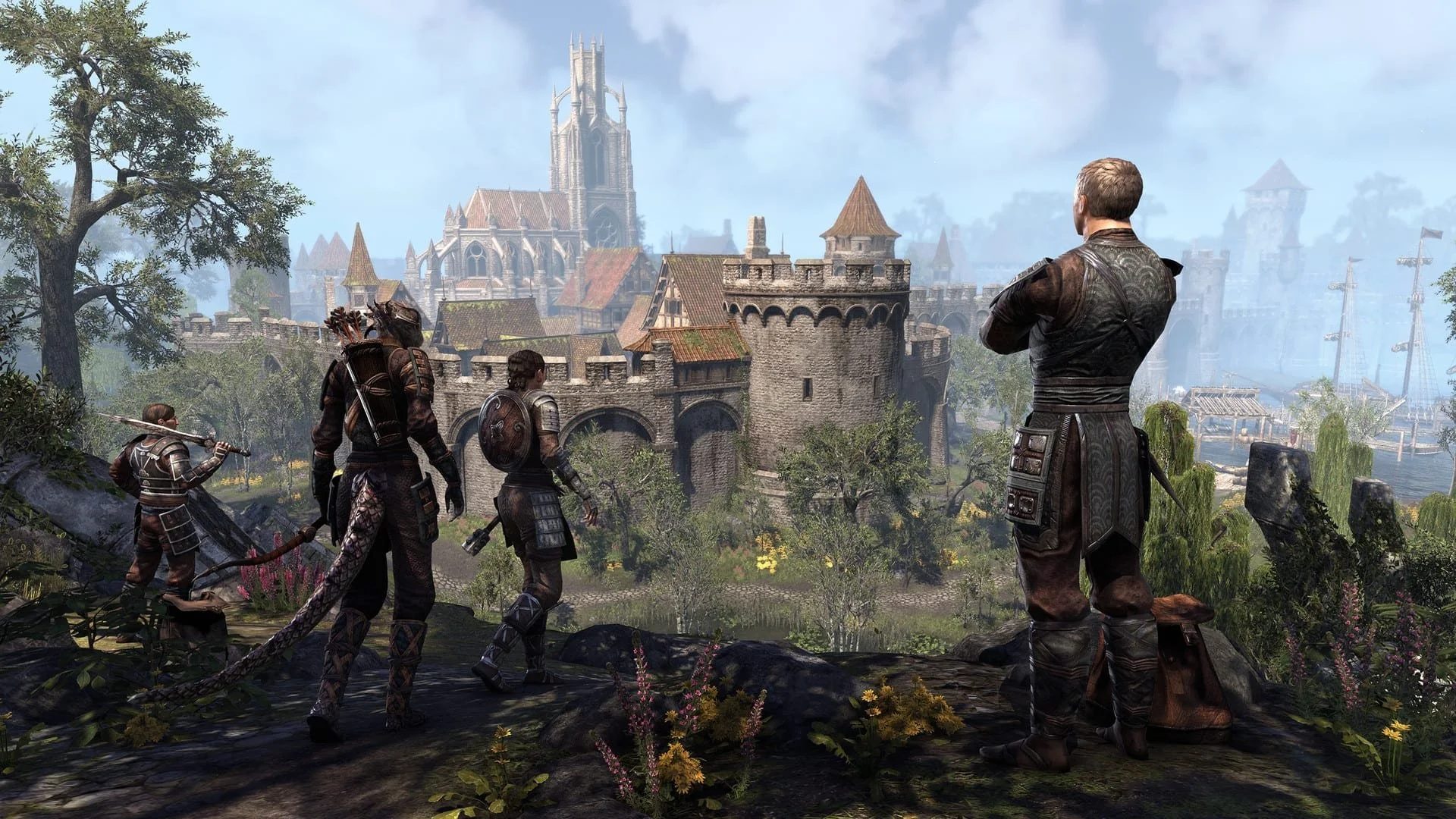 Four adventurers, two men and two women, stand on a hill overlooking a medieval castle and town, with lush trees and flowers around them.