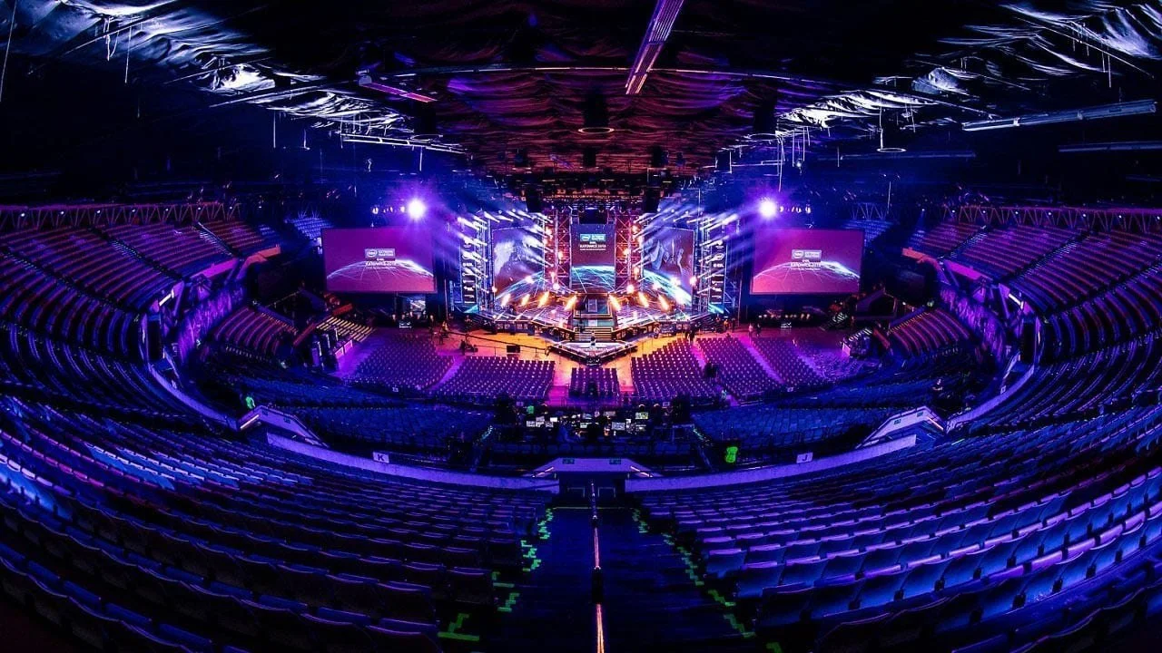 Empty concert arena with stage, large screens, and purple and blue lighting.