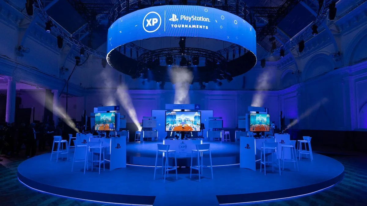 Indoor stage set up for PlayStation Tournaments with multiple screens, blue lighting, and a circular LED sign displaying XP, PlayStation, and Tournaments logos.