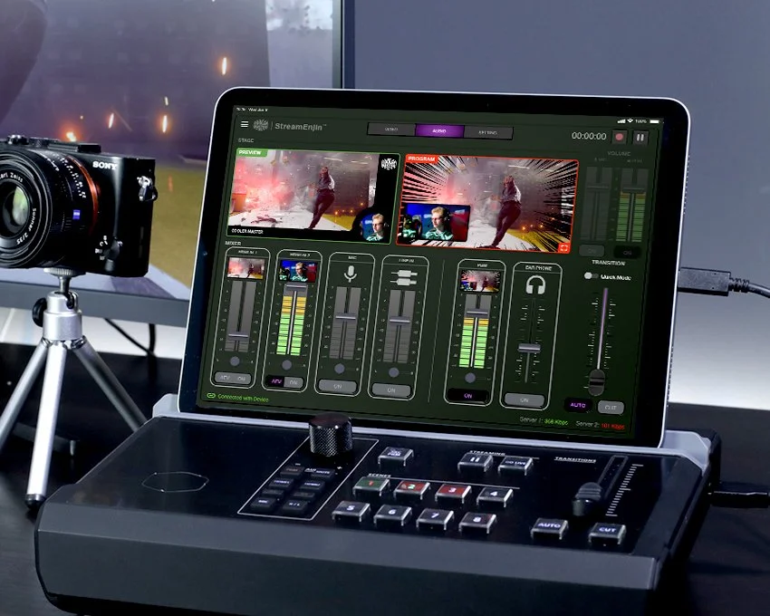 A digital video switcher and a camera on a tripod in a recording studio, with a monitor displaying video editing software.