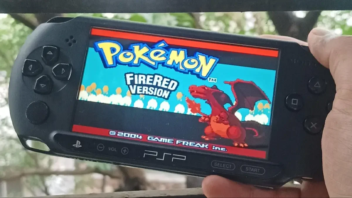 A person's hand holding a PlayStation Portable (PSP) showing the title screen of Pokémon FireRed Version.
