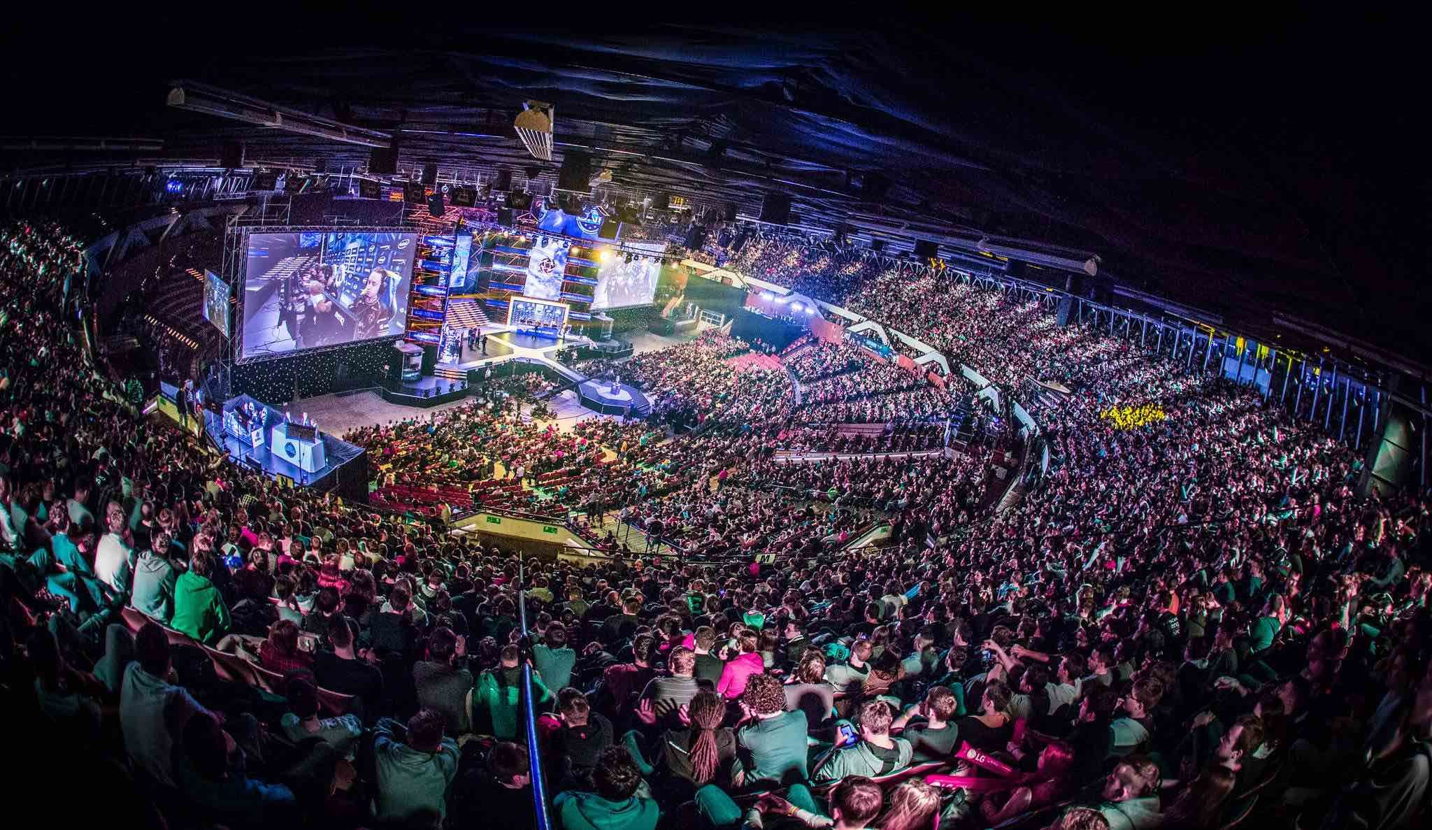 Large indoor esports arena filled with a packed audience watching a gaming tournament on big screens and stage lighting.
