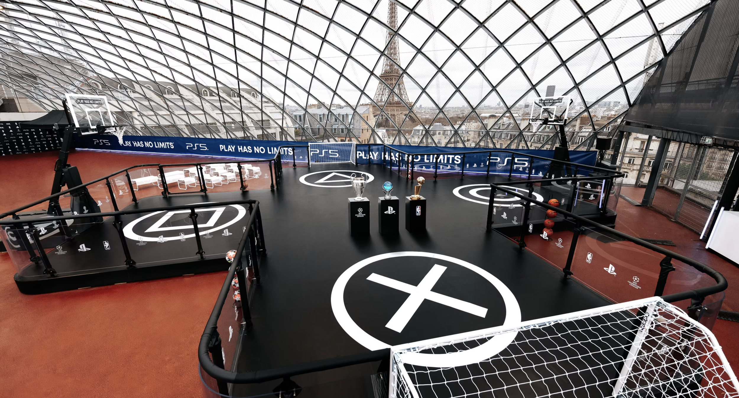 A rooftop basketball court with a glass dome ceiling, featuring multiple basketball hoops, trophy display, and Paris city skyline with the Eiffel Tower in the background.