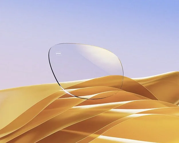 A pair of clear eyeglasses resting on golden sand dunes with a light blue sky in the background.