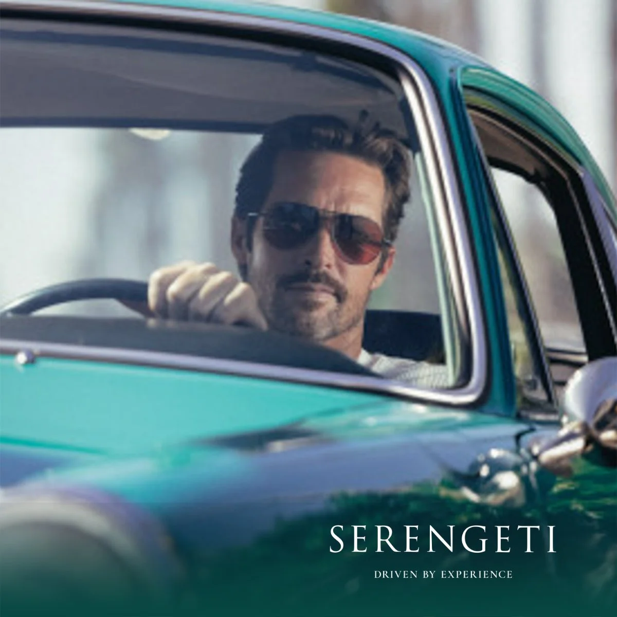 A man with dark hair and sunglasses driving a vintage green car, with the text 'Serengeti: Driven by Experience' at the bottom.