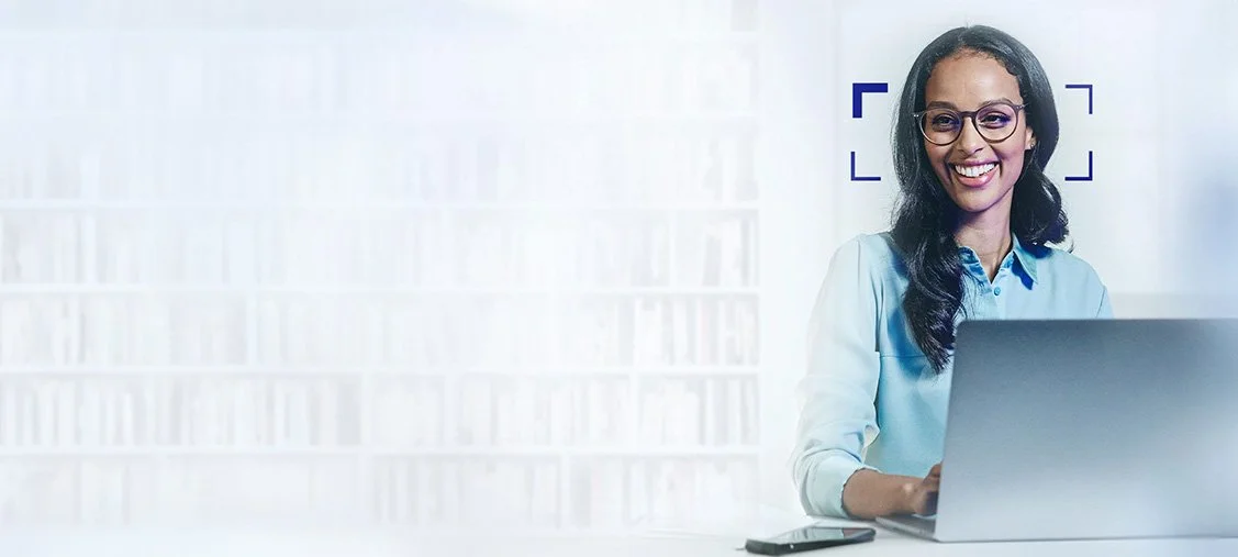 A man wearing glasses and a white shirt working at a desk with three computer monitors wearing ZEISS Office vocational progressive lenses.