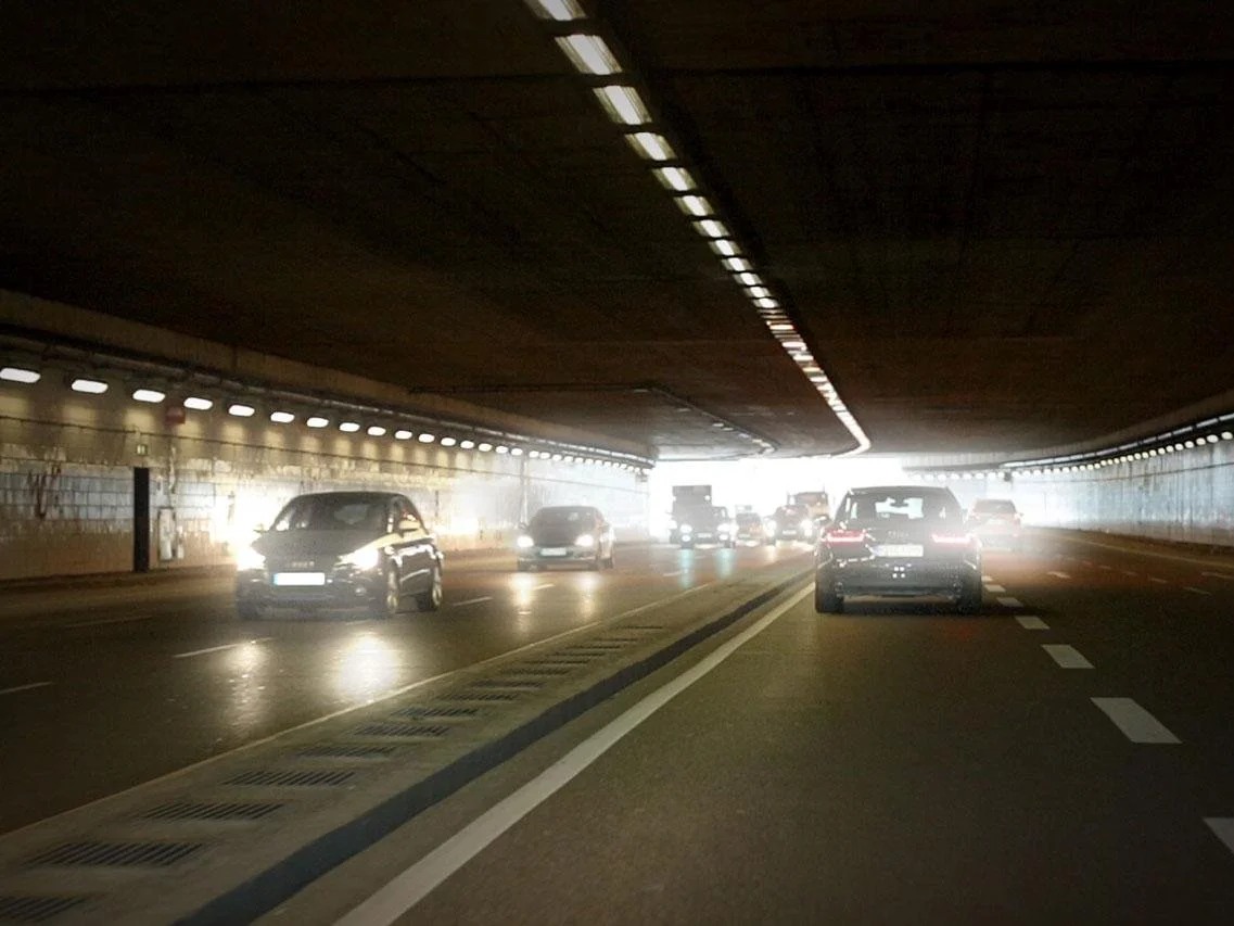 Cars driving through a tunnel with bright light at the end.