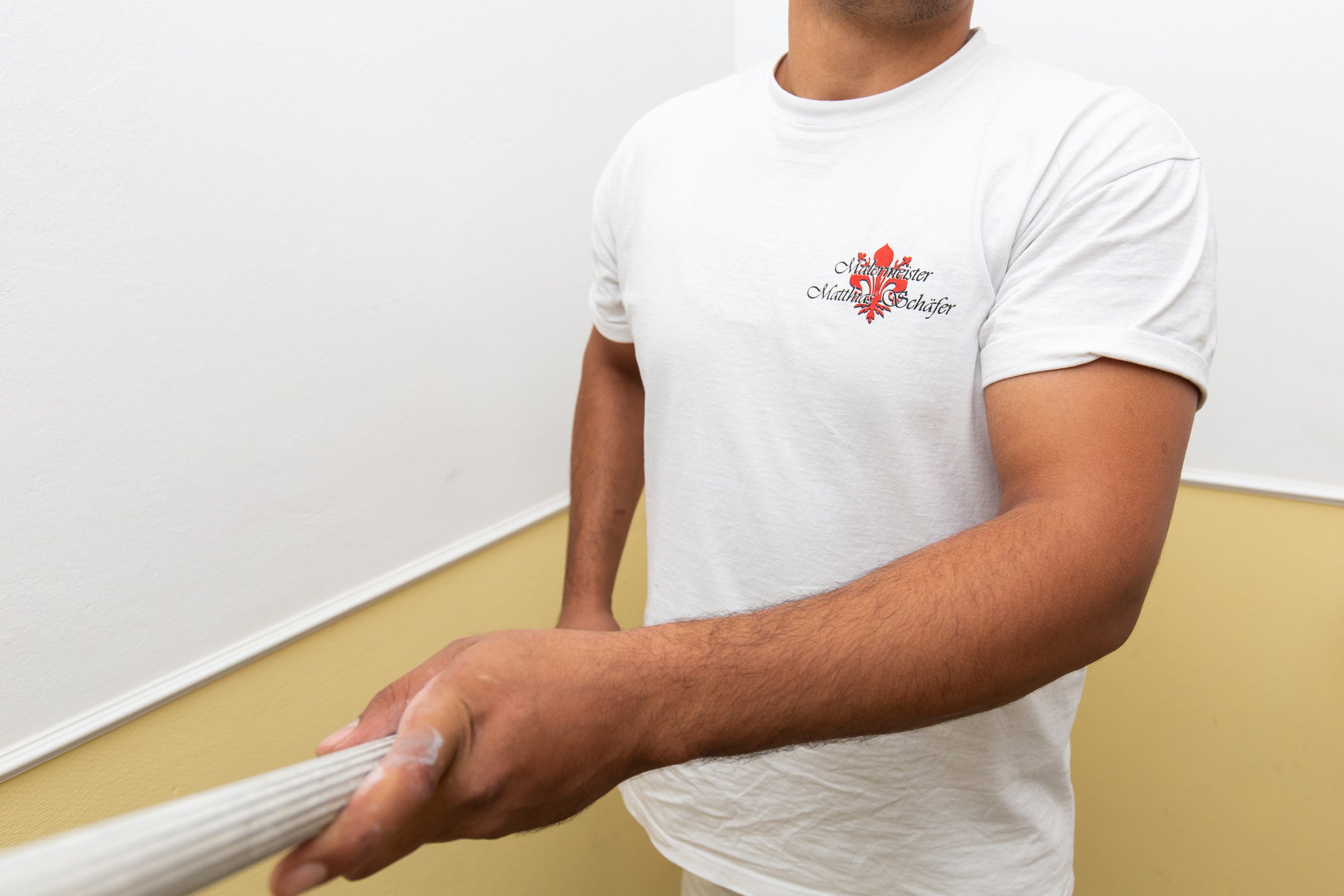 Person im weißen T-Shirt beim Streichen einer Wand, hält einen Farbroller.