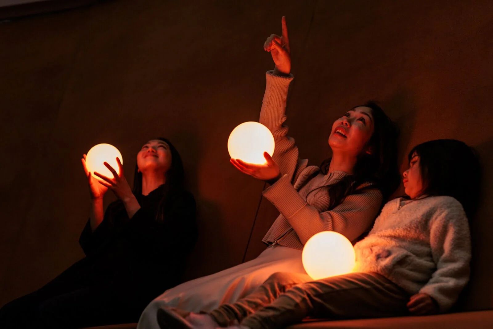 Three people holding glowing spheres, sitting in a dimly lit room.